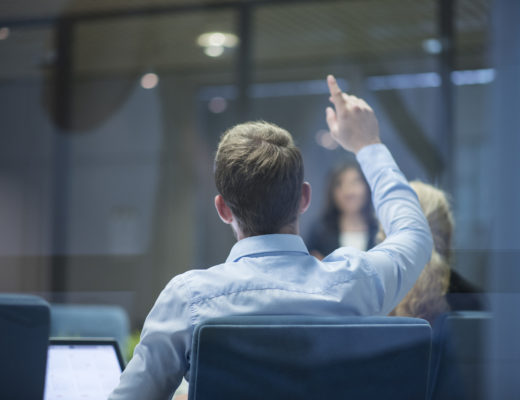 A group of businesspeople having a meeting and one businessman raising his hand with a question during the presentation