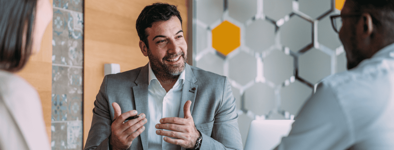A financial advisor in a business meeting explaining the benefits of CFP certification to two clients in a modern office setting.