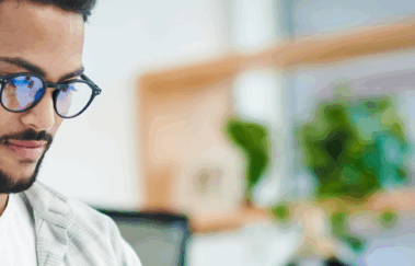 Young man wearing glasses studying on a laptop at a desk, preparing for the SIE Exam.