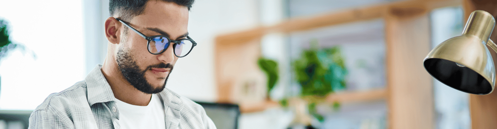 Young man wearing glasses studying on a laptop at a desk, preparing for the SIE Exam.