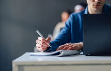 Professional studying for a FINRA qualification exam on a laptop and notebook, illustrating the updated FINRA exam retake waiting periods for SIE, Series 7, and other qualification exams.