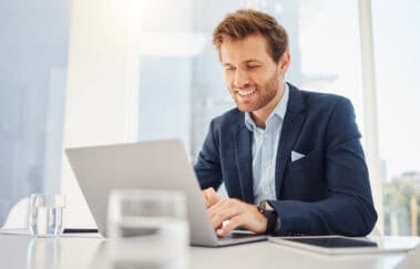 One happy young caucasian businessman working on a laptop in an office. Confident male entrepreneur planning while browsing the internet and sending emails to clients. Man joining a virtual conference via webcam