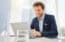 One happy young caucasian businessman working on a laptop in an office. Confident male entrepreneur planning while browsing the internet and sending emails to clients. Man joining a virtual conference via webcam
